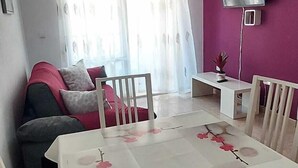 A dining area with a white table and chairs, a ceiling light, a TV mounted on the wall, and a window with curtains. - Ellite XIii Apartment Playa Naufragos Torrevieja! (Torrevieja)