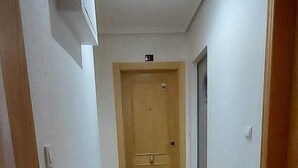 A hallway with a tiled floor, a wooden door at the end, and a light fixture on the ceiling. - Ellite XIii Apartment Playa Naufragos Torrevieja! (Torrevieja)