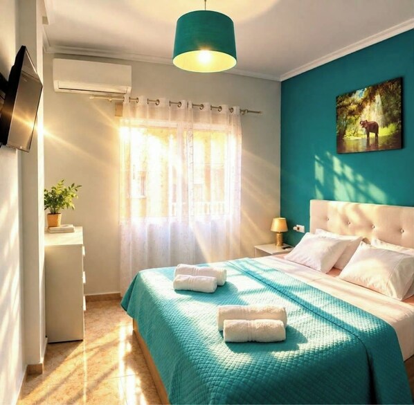 A hotel room with a bed, a television, a window with curtains, and a painting on the wall.