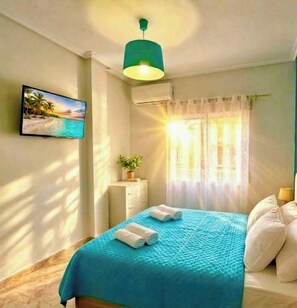 Ein Schlafzimmer mit einem Bett, einem Fernsehgerät an der Wand, einem Fenster mit Vorhängen und einer Deckenleuchte.
