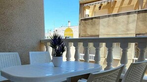 A patio with white plastic tables and chairs, a potted plant, and a view of buildings in the background. - Ellite XIii Apartment Playa Naufragos Torrevieja! (Torrevieja)