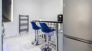 Una kitchenette pequeña con un refrigerador, una cafetera y dos taburetes azules.