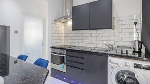 Una cocina moderna con encimera negra, salpicadero de azulejos blancos y lavadora integrada.