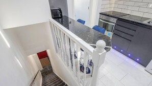 Una escalera conduce a una cocina con encimera de mármol, un tostador y una campana extractora de acero inoxidable.