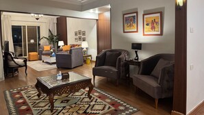 A spacious living room with a sofa, armchairs, a coffee table, and a rug. There are two lamps on side tables, and a chandelier hangs from the ceiling. - Nile View Apartment - Sleeps 4 & Balcony (Cairo)