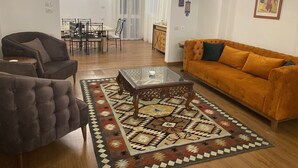 A living room with a sofa, armchair, glass coffee table, patterned rug, dining area with chairs and table, and a kitchen in the background. - Nile View Apartment - Sleeps 4 & Balcony (Cairo)