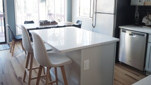 A modern kitchen with a central island, bar stools, stainless steel appliances, and a view of the outdoors through large windows. - Peaceful fully renovated chalet in Lake Harmony, dog friendly! (Lake Harmony)