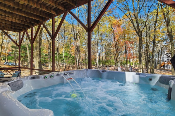 Un espace avec un bain à remous, surmonté d’une pergola en bois et entouré d’arbres aux feuilles d’automne.