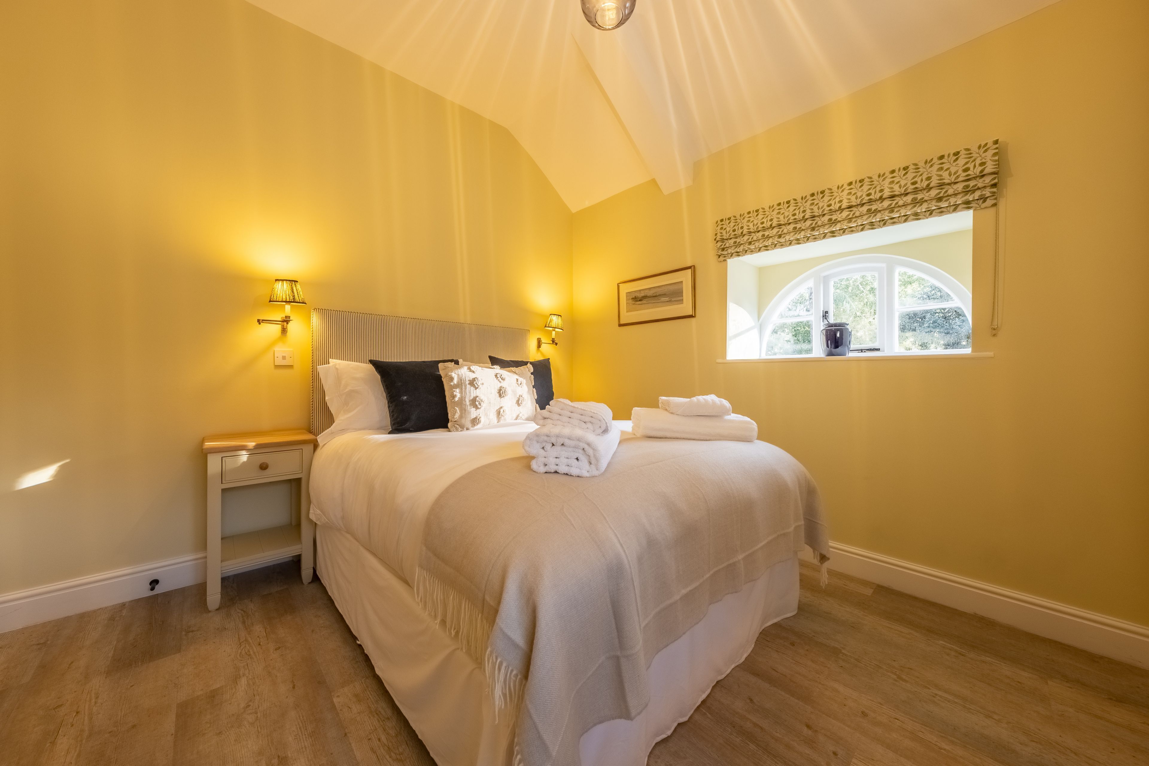 A bedroom with a bed, bedside lamps, a window with a view, and a small nightstand.