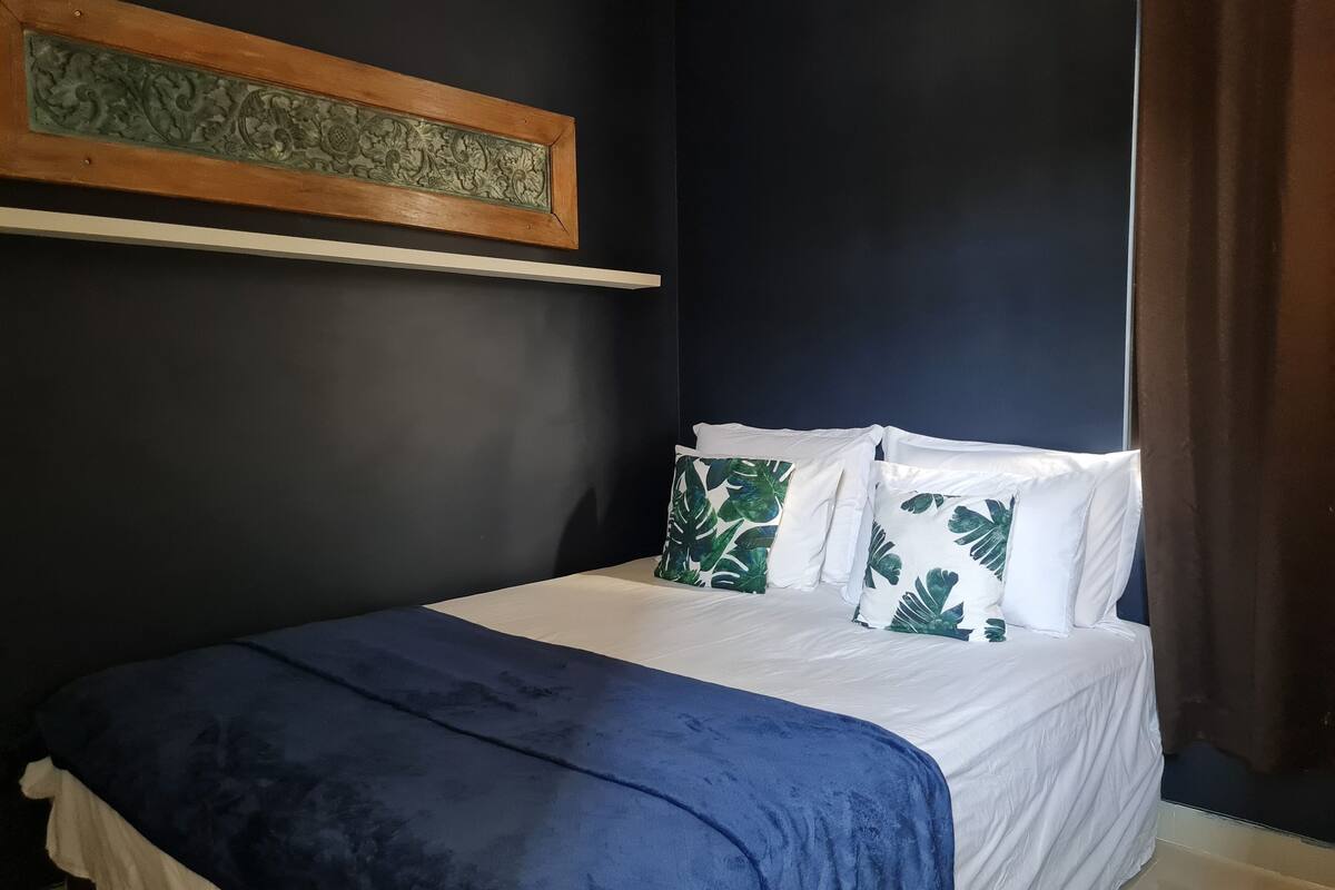 Ein Schlafzimmer mit einem Bett, weißer Bettwäsche, einer blauen Tagesdecke und Kissen mit Blättermotiv.