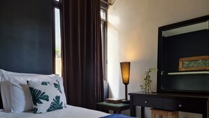 Habitació d'hotel amb llit, escriptori, làmpada i finestra amb cortines.