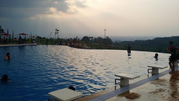 Una piscina amb gent al voltant, un cel nuvolós i una vista panoràmica d'un paisatge a la distància.
