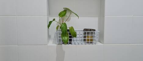 A bathroom with white tiled walls, a white shelf, and a plant in a white basket.
