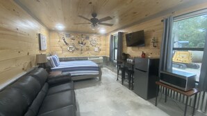 Een houten interieur van een chalet, met een bed, een bureau met een computer en een televisie.
