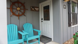 Een veranda met twee turkozen Adirondack-stoelen, een houten scheepsschijf, een bord met 'Pirates Cove' en een deur met het nummer 280.