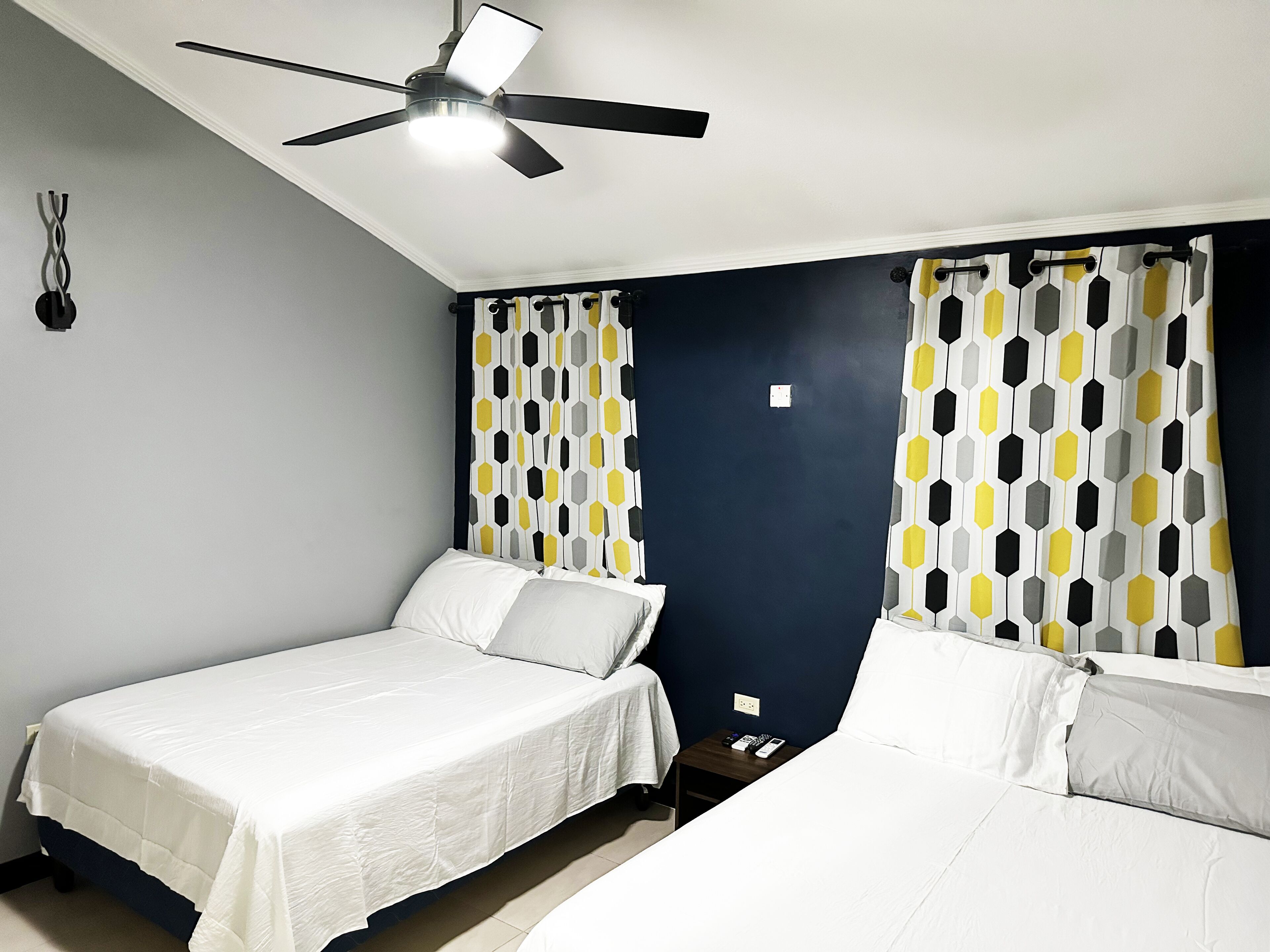 A hotel room with two single beds, a ceiling fan, and patterned curtains.