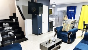 Una sala de estar moderna con una escalera, un televisor de pantalla plana, un comedor y una cocina.