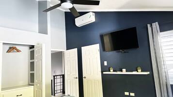 A bedroom with a bed, a ceiling fan, a TV, and a window with curtains.
