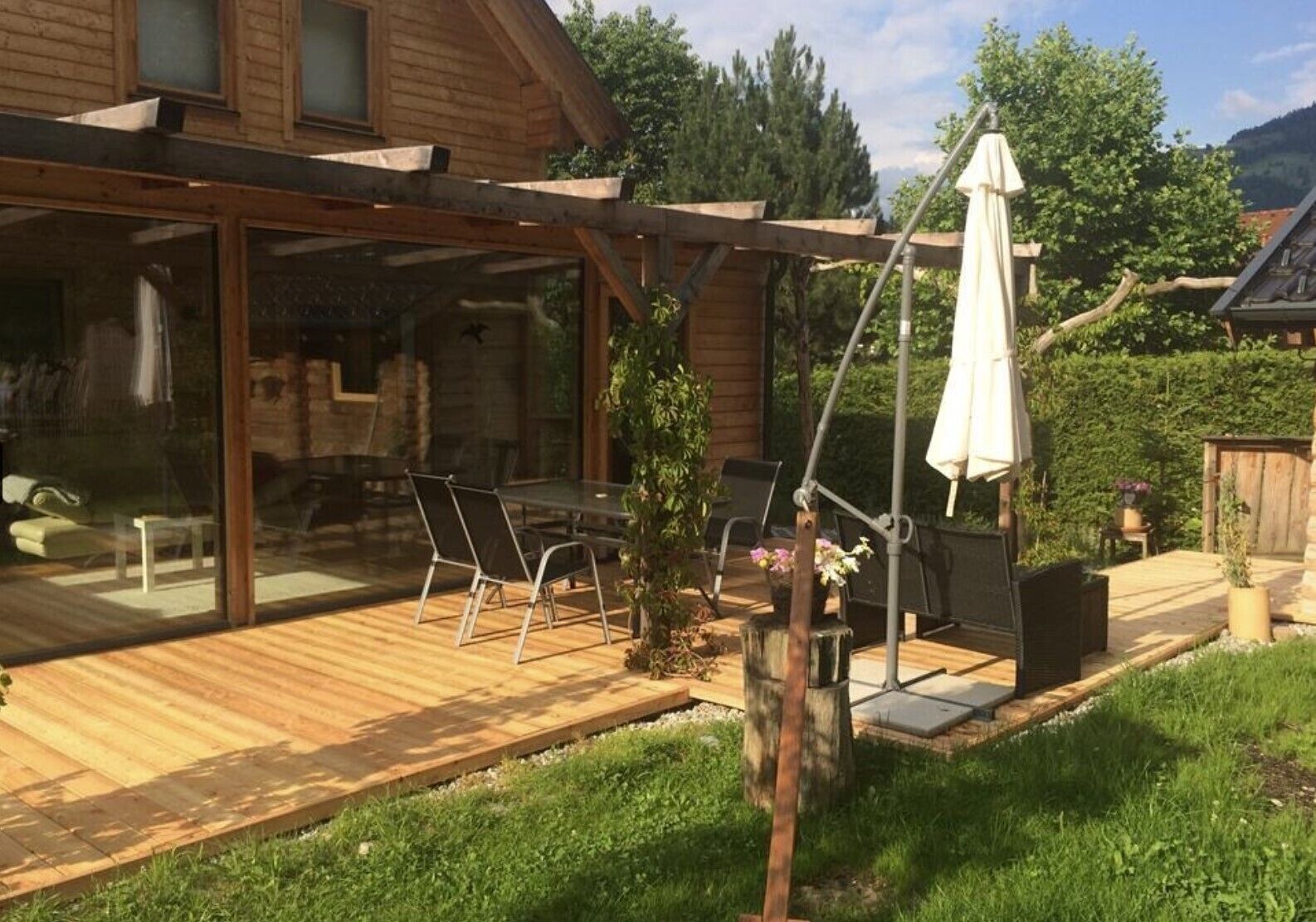 Une terrasse en bois avec des meubles d’extérieur, une pergola et un grand parasol.