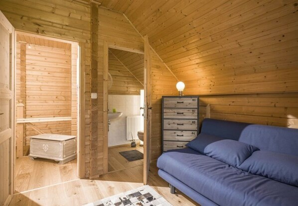 A wooden cabin interior with a blue sofa, a dresser with drawers, and a radiator in the bathroom.