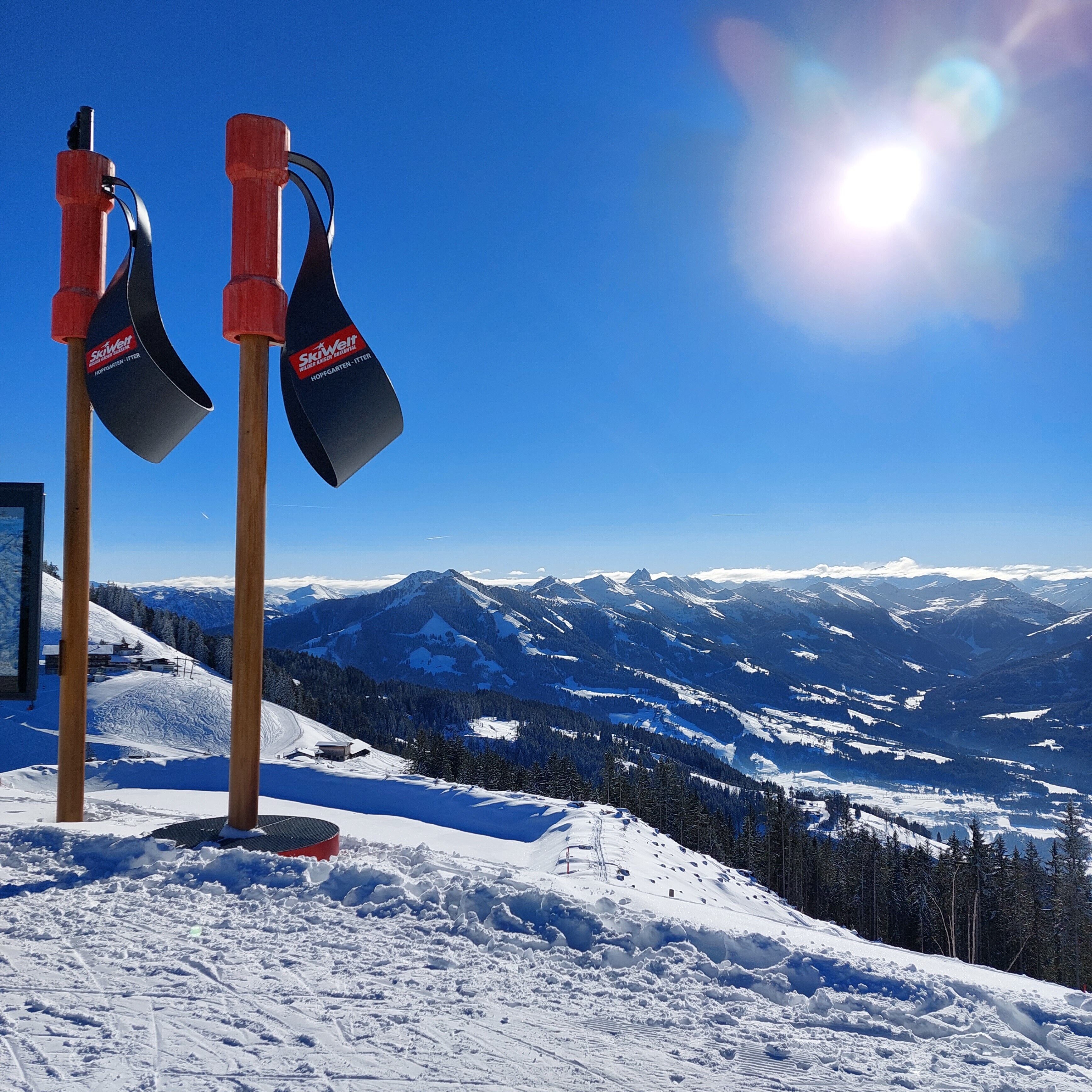 A snowy mountain landscape with a clear sky and two ski poles with 'SkiWell' branding.