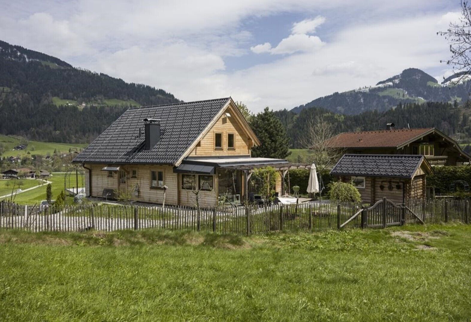 A wooden house with a sloped roof, a covered porch, and a fenced yard.