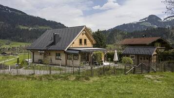 A wooden house with a sloped roof, a covered porch, and a fenced yard.