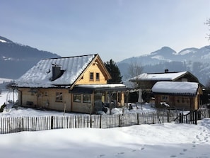 Ein Holzhaus mit geneigtem Dach, umgeben von einem Holzzaun, vor einer Berglandschaft.