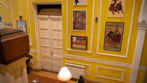 A hallway with yellow walls, white trim, and a closed door. There are framed pictures and a poster on the wall. - Sevilla home Hotel (Buenos Aires)