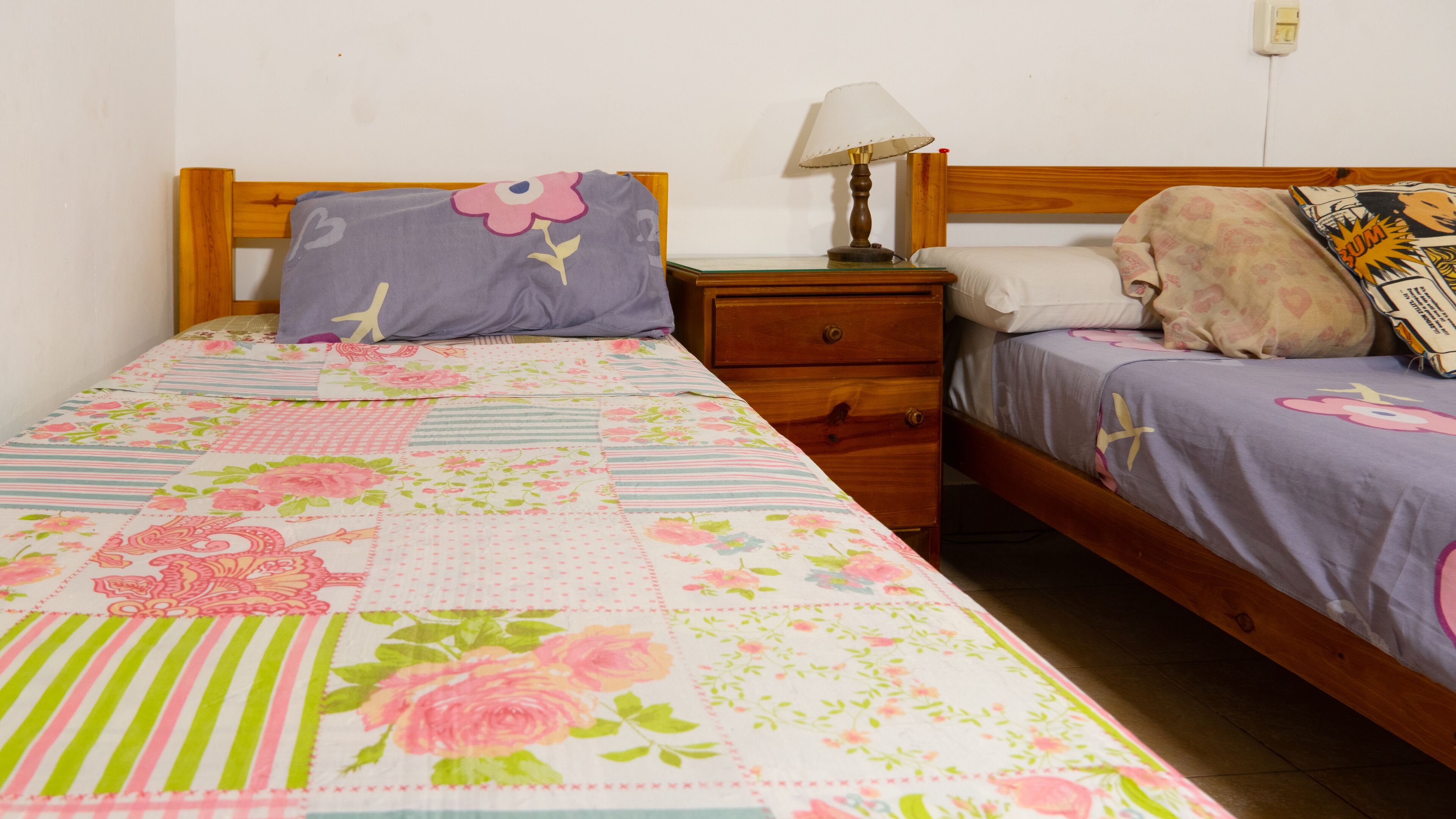 A bedroom with a wooden bed frame, a nightstand with a lamp, and a dresser.
