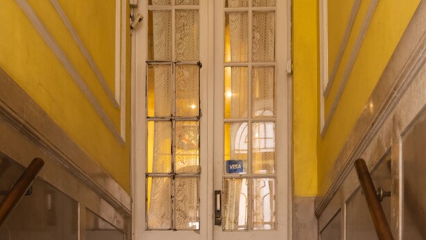 A staircase leading to a double door with a Visa sign, flanked by yellow walls and wooden handrails. - Sevilla home Hotel (Buenos Aires)