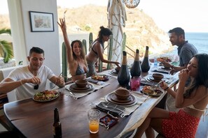A group of people dining at an outdoor table with a view of the ocean.