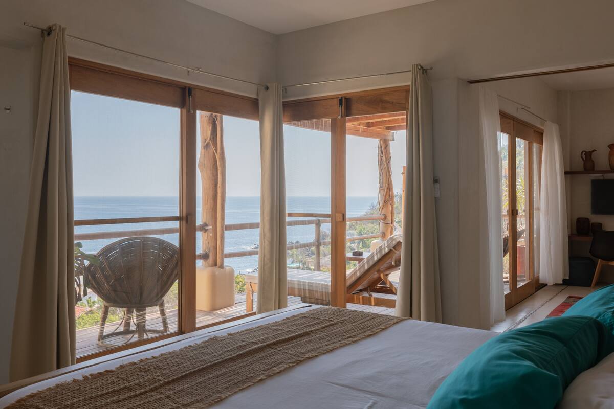 Un dormitorio con un ventanal grande, una cama y vistas al mar.