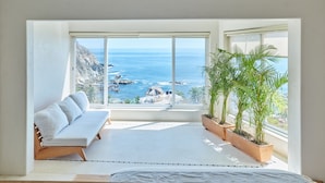 Uma varanda com sofá branco, plantas em vasos e vista para o oceano.