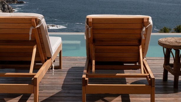 Duas poltronas de madeira viradas para um deck de madeira com vista para o oceano.