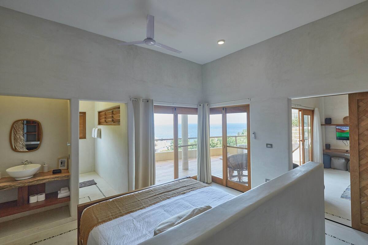 Un dormitorio con una cama grande, un baño con lavamanos y un balcón con vistas.