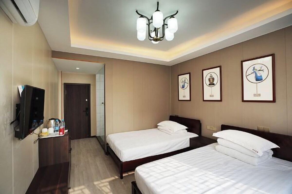 A hotel room with two beds, a TV, a minibar, and artwork on the walls.