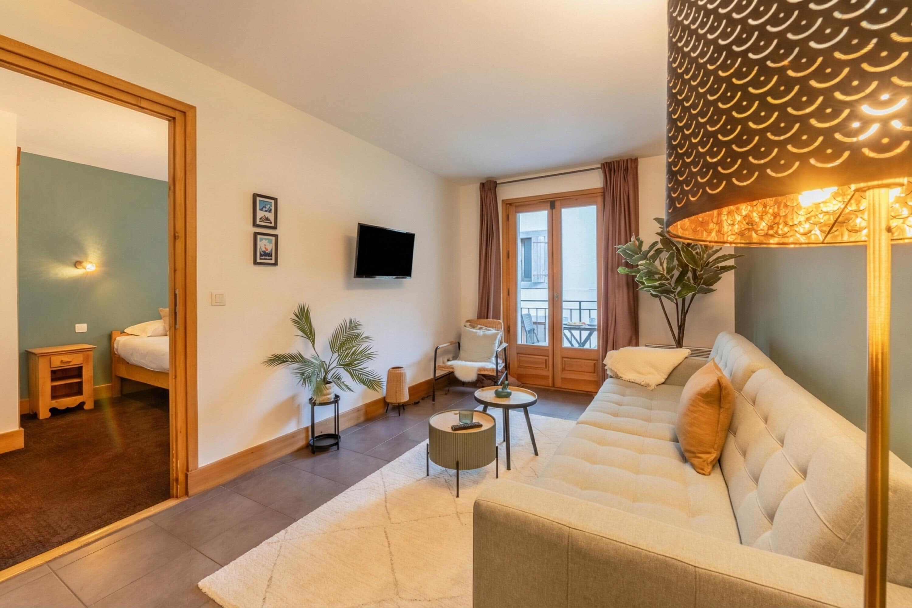 Una sala de estar con sofá, televisión, lámpara y puerta al balcón.