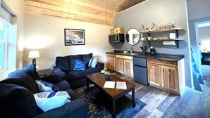 Una sala de estar moderna con sofá, mesa de centro y comedor, con una cocina al fondo.