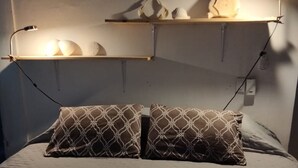 Uma cama com travesseiro estampado e uma prateleira acima com objetos decorativos.