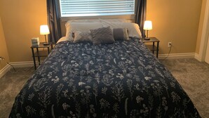 Un dormitorio con una cama, dos lámparas de noche, una ventana con persianas y suelo alfombrado.