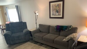 Una sala de estar con un sofá gris, un sillón gris, un tapete color beige, una lámpara de pie y un cuadro en la pared.
