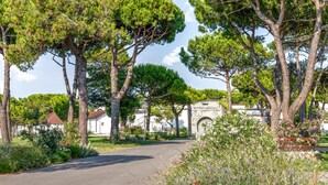 A paved road flanked by trees and flowering plants, leading to a building with a stone archway and a sign reading "BATTERIA C.A.R.A.DUCCI". - Nice home in Cavallino-Treporti (Cavallino-Treporti)