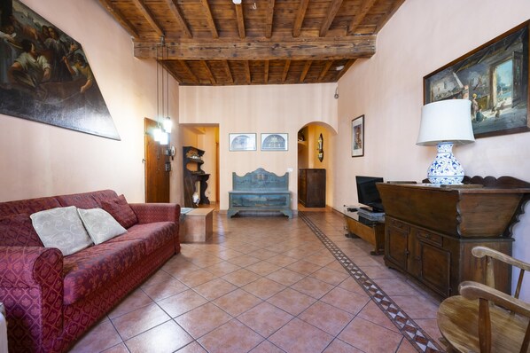A cozy living room with a red sofa, wooden furniture, and a tiled floor.