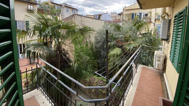 Un balcón con vistas a un patio interior, con barandilla de metal y plantas en macetas.