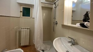 Un baño con ducha, lavamanos, bidé, toallero, espejo y una lámpara en el techo.