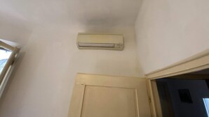 Una habitación con techo blanco, puerta color beige y aire acondicionado instalado en la pared.
