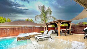 Patio con piscina, bañera de hidromasaje y zona de estar al aire libre bajo una pérgola.