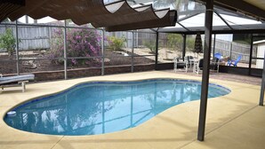 A swimming pool with a curved edge, surrounded by a covered patio area with chairs and a table. - 3bed/2bath pool home, sleeps 8 guests, great location, private/sunny aspect. (Davenport)