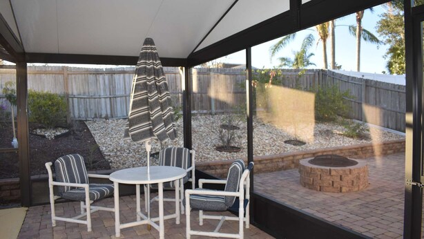A covered patio area with a table and chairs, a striped umbrella, and a view of a backyard with a wooden fence and landscaping. - 3bed/2bath pool home, sleeps 8 guests, great location, private/sunny aspect. (Davenport)